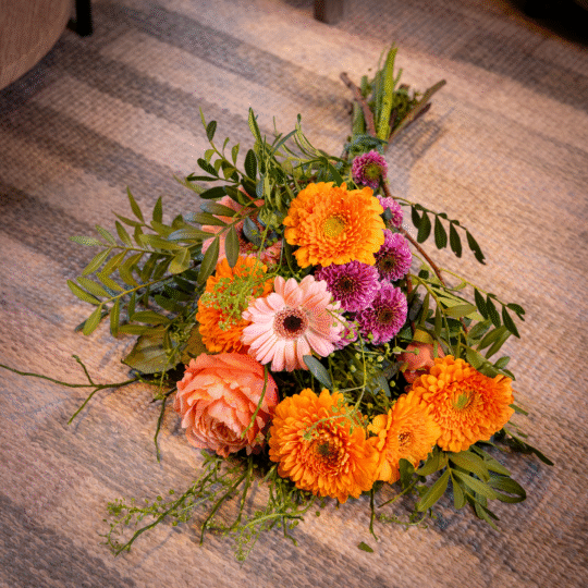 Bukett med orange dahlior, rosa germini, lila krysantemum, persikofärgad ros och säsongens gröna bladverk.
